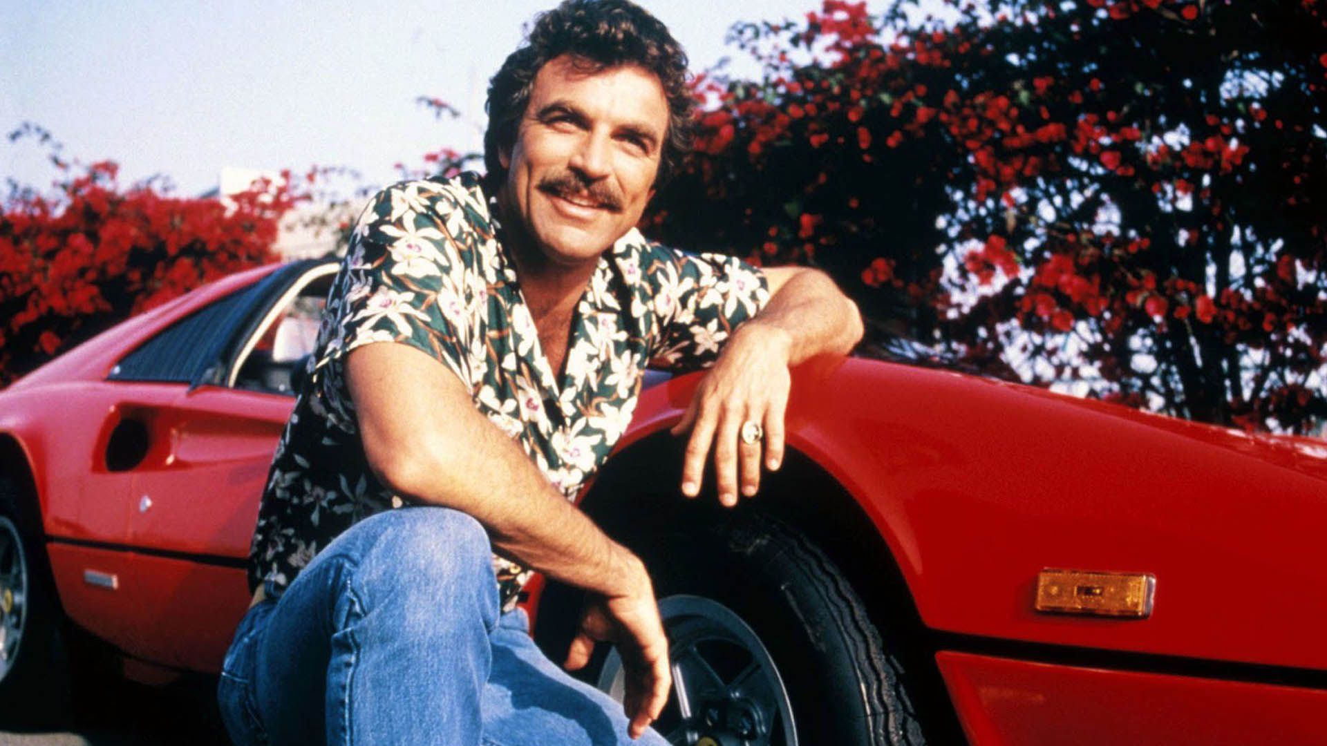شخصیت اصلی سریال magnum pi با بازی تام سلک در کنار یک ماشین فراری قرمز
