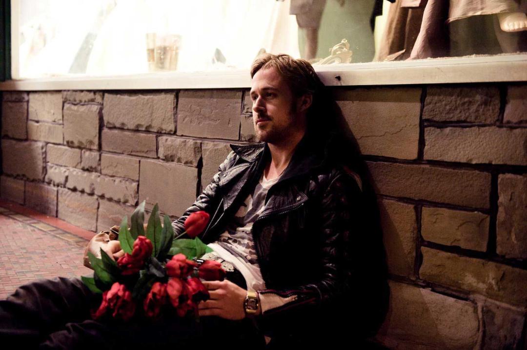 تکیه دادن رایان گاسلینگ جوان به دیوار در حال نگه داشتن گل های قرمز در فیلم Blue Valentine