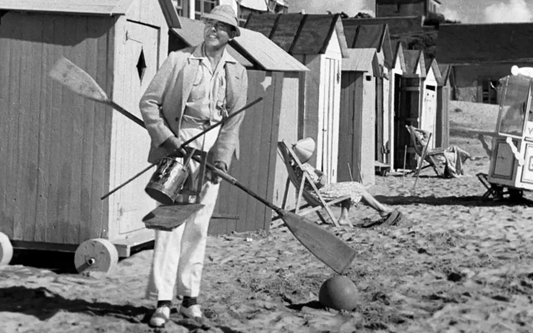 فیلم Monsieur Hulot's Holiday از سینمای فرانسه و مرد کلاه دار مشغول حمل دو پاروی قایق روی ماسه