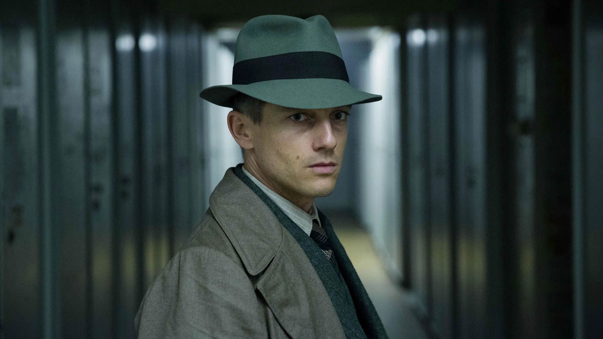 فولکور بروخ در نقش شخصیت اصلی با کلاه و بارانی در راهروی سریال Babylon Berlin ایستاده است
