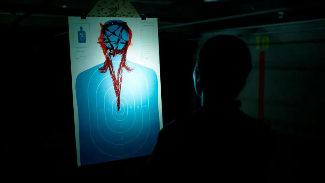 یک افسر پلیس ایستاده در تاریکی مقابل یک صفحه‌ی تمرین تیراندازی که با نور چراغ قوه قابل رویت است و روی آن طرحی خونین دیده می‌شود در نمایی از فیلم شیطانی به کارگردانی آنتونی دی‌بلاسی