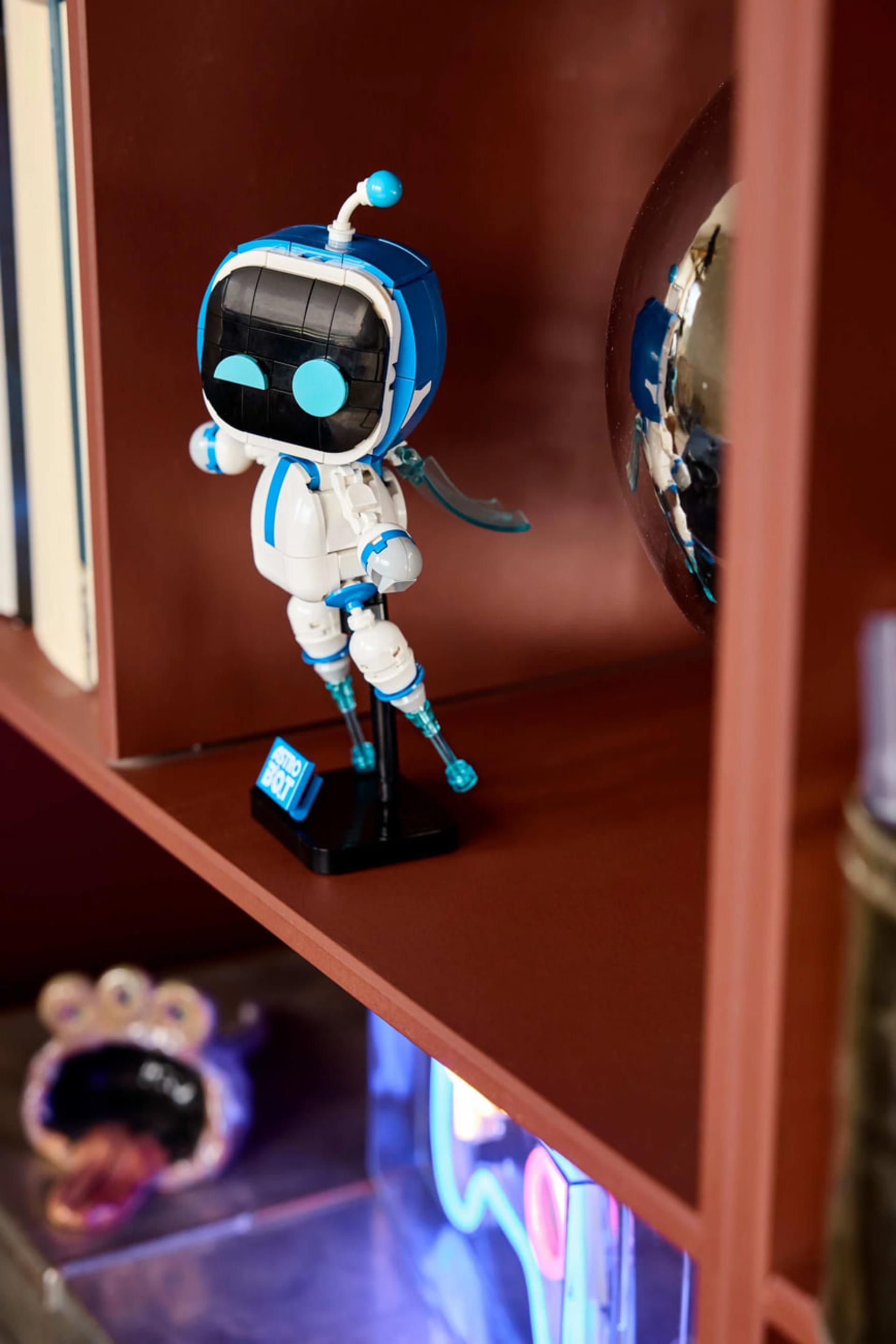 فیگور کوچک ربات استرو بات (Astro Bot) روی قفسه چوبی