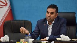 مردی با کت و شلوار رسمی در حال صحبت در یک جلسه رسمی در مقابل پرچم ایران