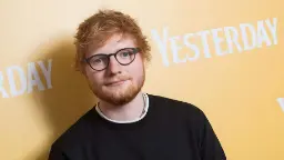 اد شیرن (Ed Sheeran) با عینک و لباس مشکی در مقابل پس‌زمینه زرد