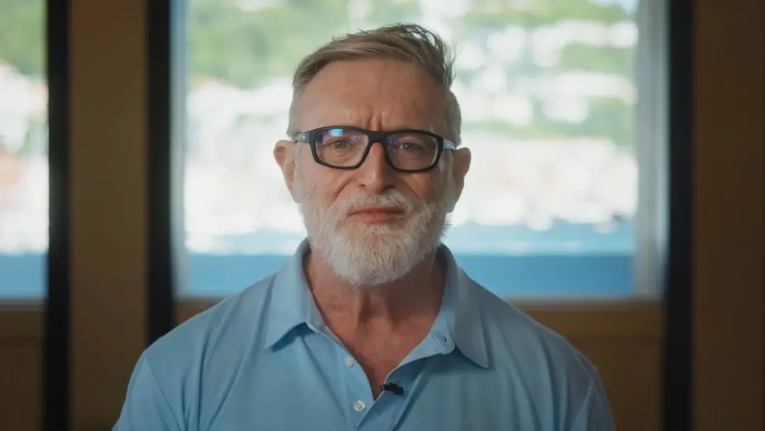 گیب نیوئل (Gabe Newell) با عینک و پیراهن آبی در مقابل پنجره