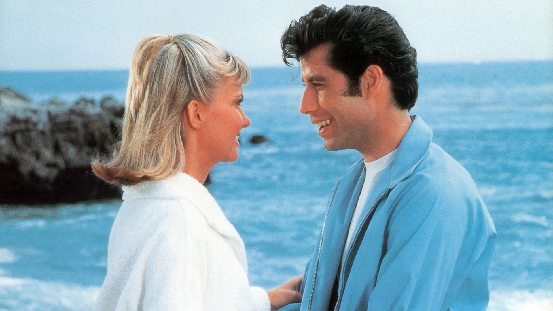 grease_man_in_blue_smiling_at_a_girl_near_the_sea