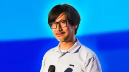 هیدئو کوجیما (Hideo Kojima) با عینک سیاه در مقابل پس‌زمینه آبی