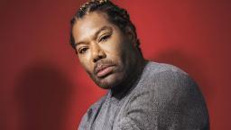 صداپیشه کریتوس (Christopher Judge) با موهای بافته شده در مقابل پس‌زمینه قرمز