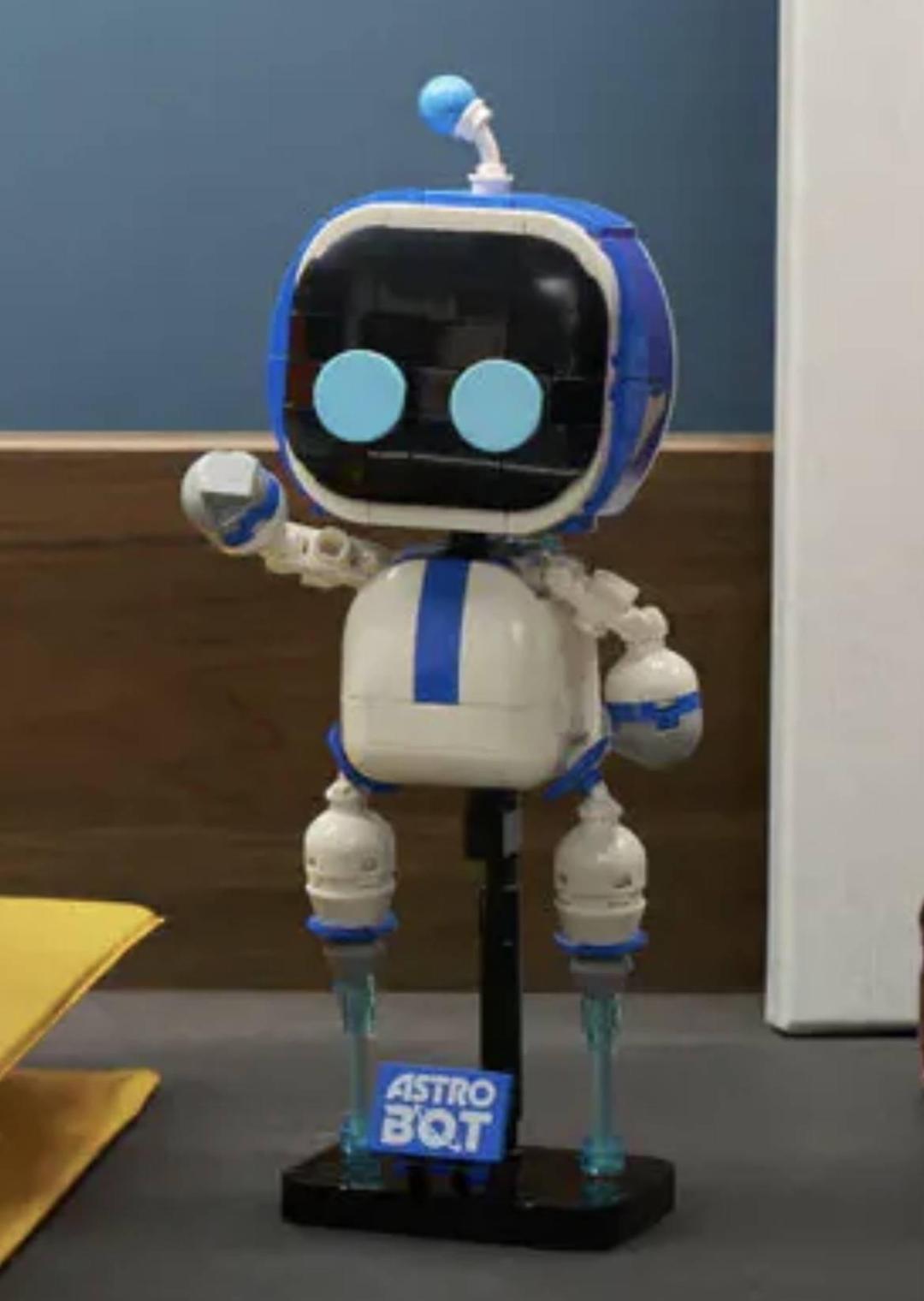 عروسک لگو آسترو بات (Astro Bot) با بدنه سفید و آبی روی پایه ایستاده