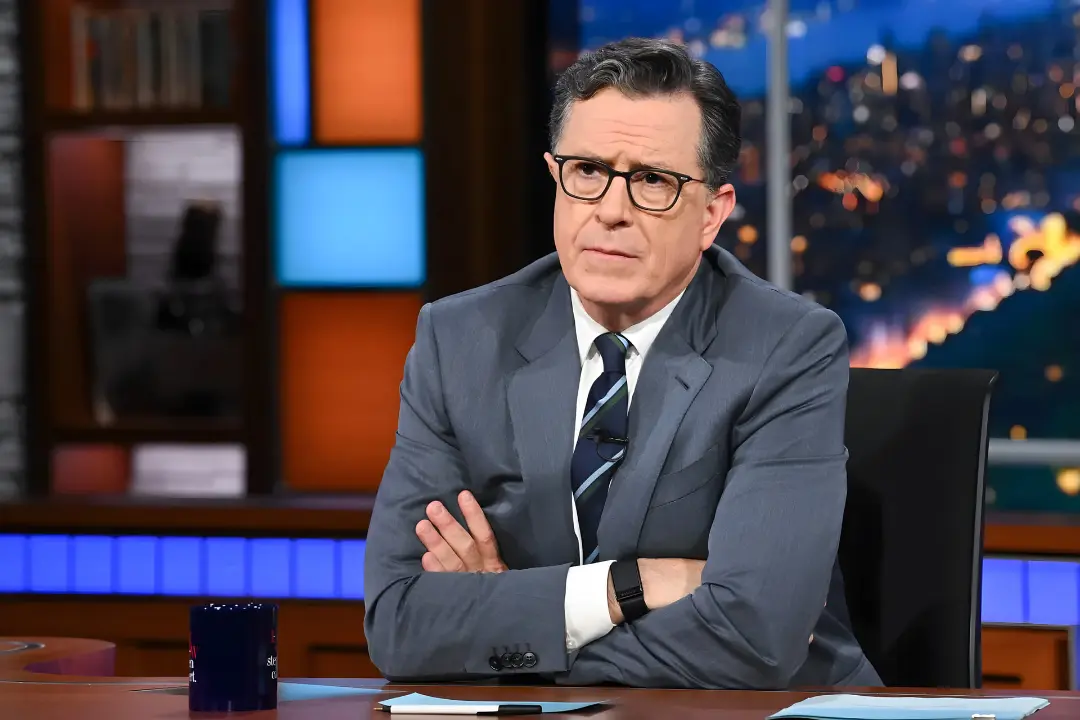 استیون کولبر (Stephen Colbert) با عینک و کت خاکستری در استودیو