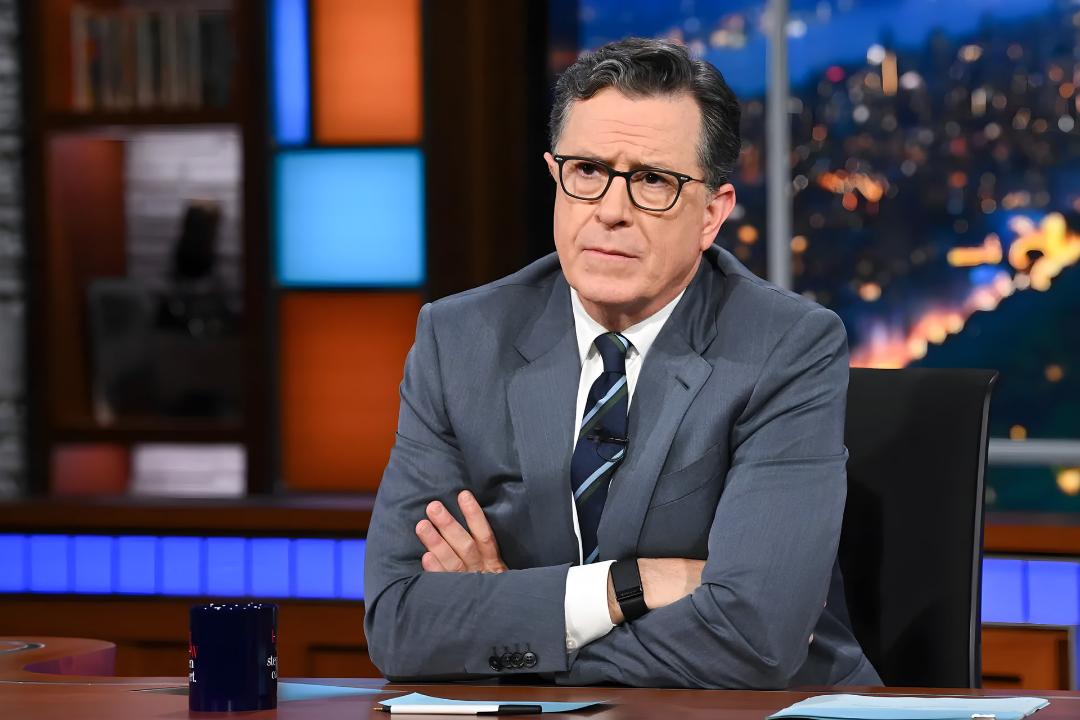 استیون کولبر (Stephen Colbert) با عینک و کت خاکستری در استودیو