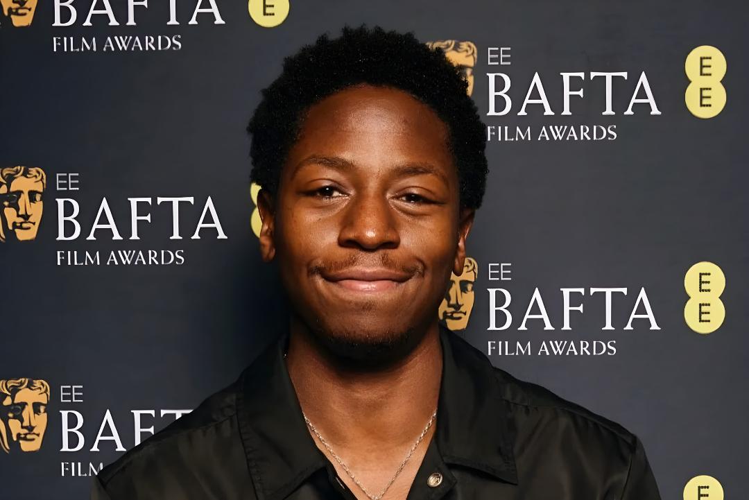تصویر چهره یک مرد جوان با لبخند ملایم در مقابل پس‌زمینه لوگوی جوایز فیلم BAFTA